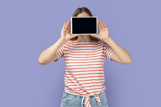 Mujer que cubre la cara con una tableta con espacio de copia de pantalla vacío para texto promocional