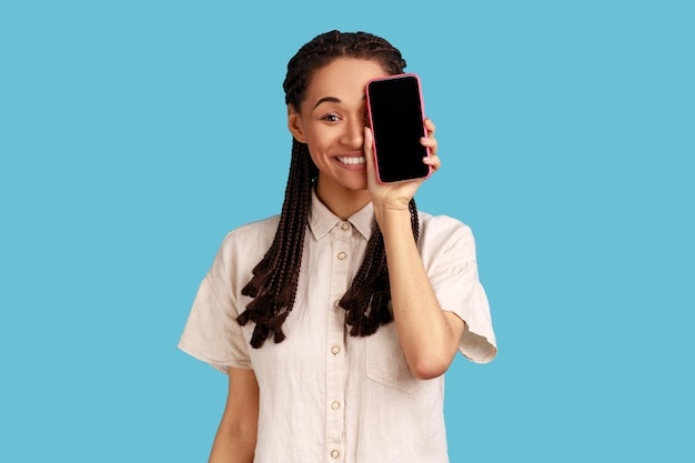 Mujer que cubre la mitad de la cabeza con el teléfono móvil ocultando el ojo con el teléfono celular y sonriendo a la cámara