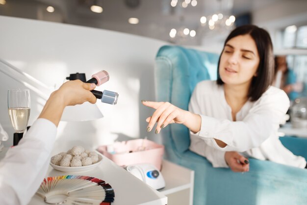 Mujer que elige el esmalte de uñas en el salón de belleza, procedimiento de manicura y pedicura.