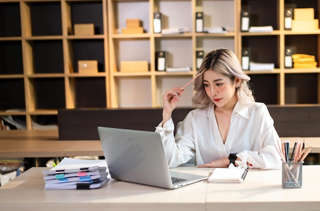 Mujer que está cansada y pensando demasiado por trabajar con tableta y computadora portátil en officexA