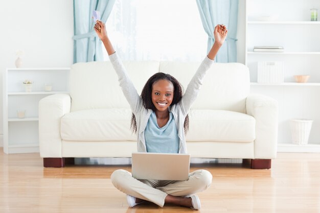 Mujer que estira mientras que se sienta en el piso que trabaja en la computadora portátil