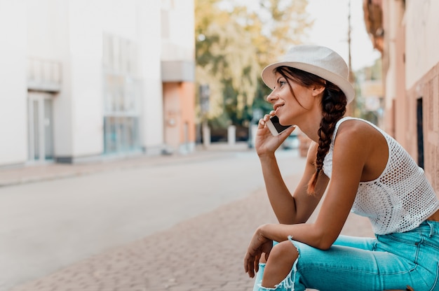 Foto mujer que habla por el teléfono al aire libre en el sombrero blanco que lleva de la calle de la ciudad.