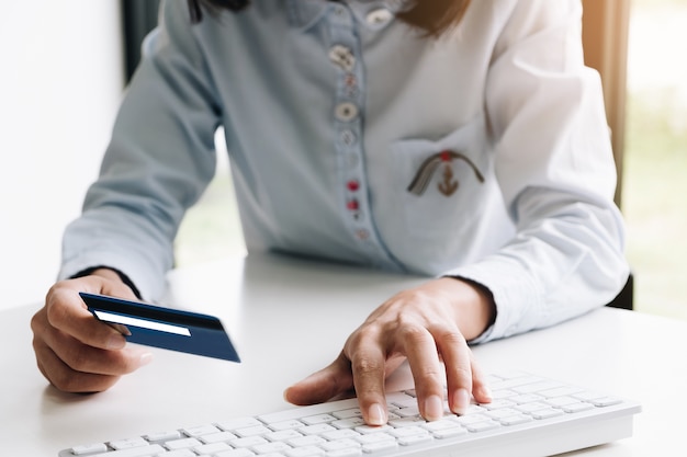 Mujer que hace el pago en línea en el teléfono móvil inteligente y la computadora portátil con tarjeta de crédito