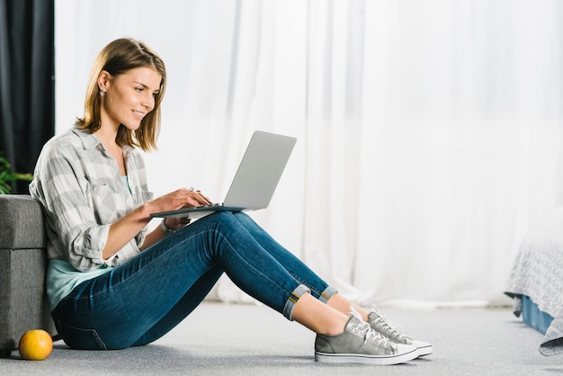 Mujer que hojea la computadora portátil en piso