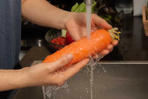 Mujer que lava verduras en la encimera cerca del fregadero en el interior de una cocina moderna