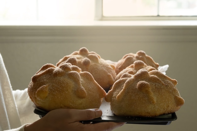 Mujer que lleva la bandeja con pan de muerto delante de la ventana, con espacio de copia