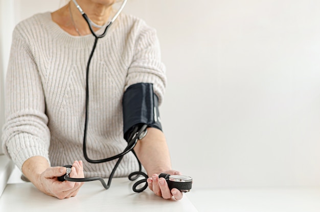 Foto mujer que mide la presión arterial sola en casa con un dispositivo manual. autocuidado y concepto médico.