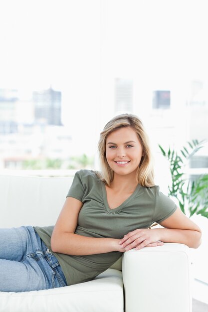 Mujer que miente en el sofá, brazos en el resto del brazo, sonriendo y mirando hacia adelante