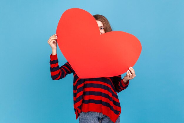 Una mujer que mira furtivamente desde un gran corazón rojo es tímida para expresar sus sentimientos románticos y su amor