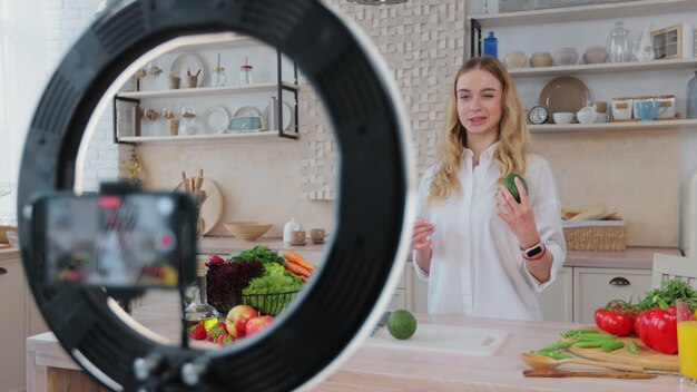 Mujer que muestra cómo cocinar alimentos saludables y grabar un blog con un teléfono inteligente en la cocina Crear contenido publicado en las redes sociales Concepto de influencer