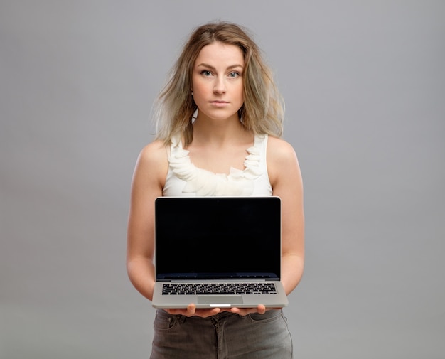 Mujer que muestra la pantalla de la computadora portátil en blanco