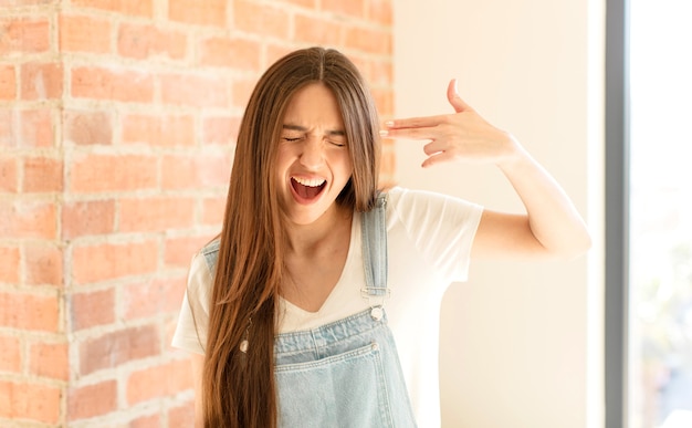 Mujer que parece infeliz y estresada, gesto de suicidio haciendo un signo de pistola con la mano, apuntando a la cabeza