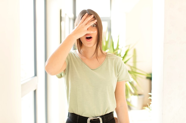 mujer que parece sorprendida, asustada o aterrorizada, cubriendo la cara con la mano y mirando entre los dedos