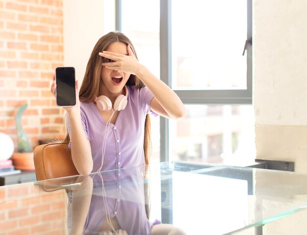 mujer que parece sorprendida, asustada o aterrorizada, cubriendo la cara con la mano y mirando entre los dedos