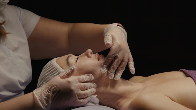 Mujer que recibe un masaje facial antienvejecimiento en el salón de spa relax Bienestar cuidado de la piel del cuerpo tratamiento de belleza facial Fondo negro
