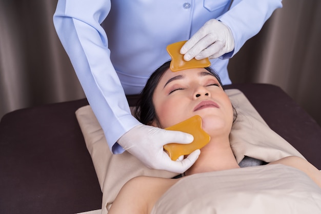 Mujer que recibe terapia facial tradicional de guasa