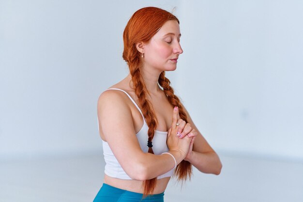 Mujer que respira con calma con los ojos cerrados y las manos en la postura namaste practica el ejercicio de yoga en la clase de estudio