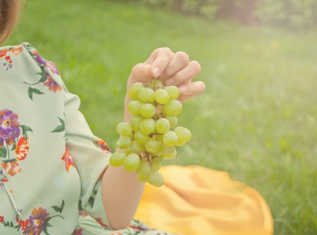 Mujer que se sienta en la cubierta amarilla y que sostiene el racimo de uvas.