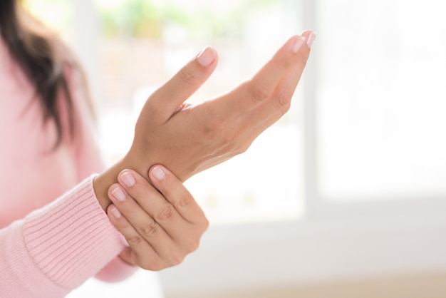 Foto la mujer que se sienta en el sofá lleva a cabo su lesión de la mano de la muñeca, sintiendo dolor.