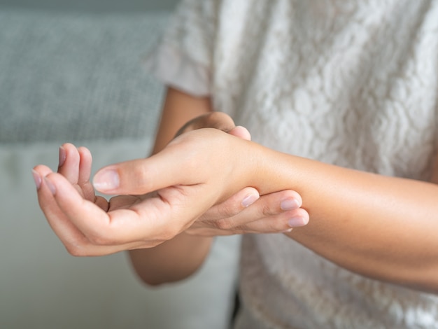 La mujer que se sienta en el sofá sostiene su muñeca. lesión en la mano