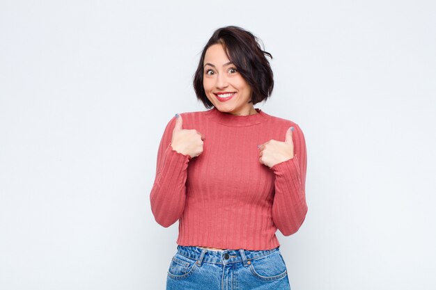 Mujer que se siente feliz, sorprendida y orgullosa, apuntando a sí misma con una mirada emocionada y asombrada