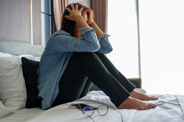 Mujer que se siente sola, deprimida y estresada, sentada con la cabeza entre las manos en el dormitorio oscuro de la sala de estar del hogar, el concepto de salud mental y la emoción negativa