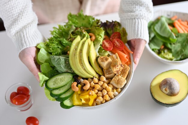 Una mujer que sirve un delicioso tazón de Buda saludable o una ensalada verde mezclada con tofu a la parrilla