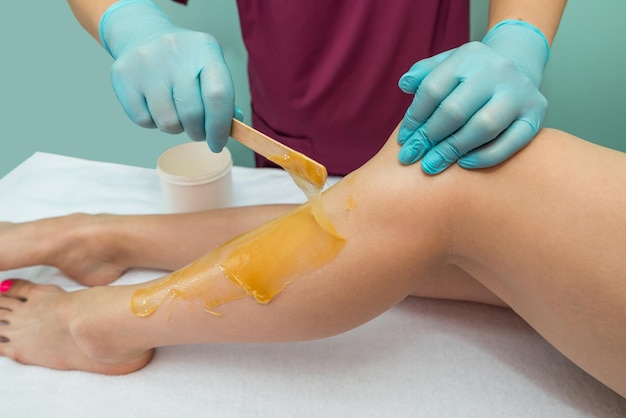 Mujer que se somete a un procedimiento de depilación de piernas con pasta de azúcar en el salón Cuidado de la piel eliminar el vello con pasta de azúcar