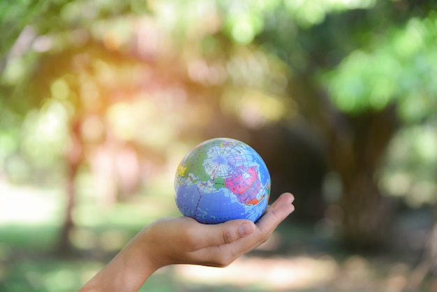 Mujer que sostiene la bola del mundo en su mano con el fondo verde natural. Concepto del día mundial del medio ambiente.