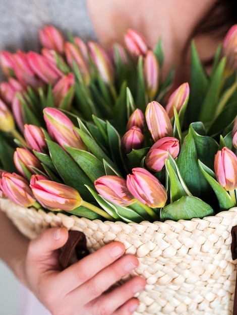 Mujer que sostiene el bolso de la paja con el manojo de tulipanes rosados frescos