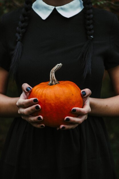 Mujer que sostiene la cosecha de otoño de la calabaza naranja