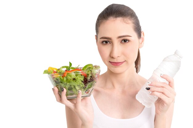 Mujer que sostiene la ensalada de verduras fresca en recipiente de vidrio sobre fondo blanco