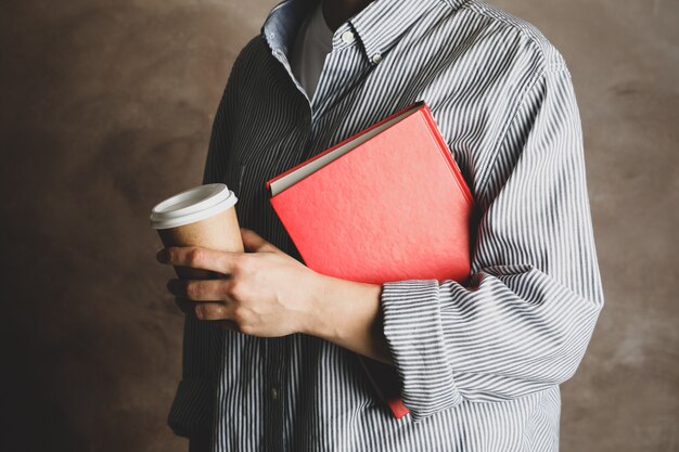 Mujer que sostiene el libro y el café contra el fondo marrón, cierre