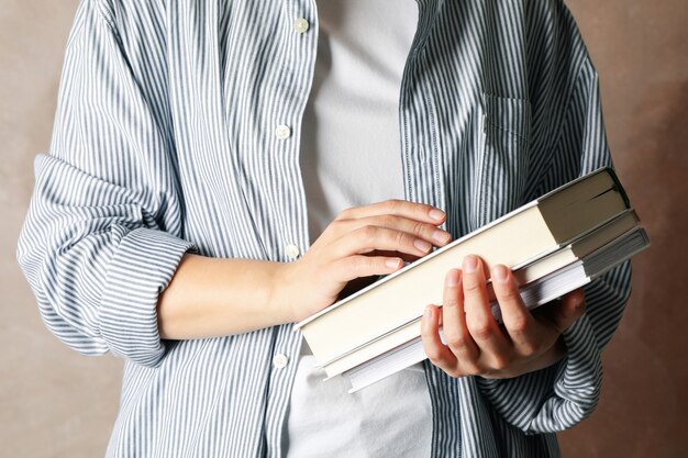 Mujer que sostiene los libros contra el fondo marrón, cierre