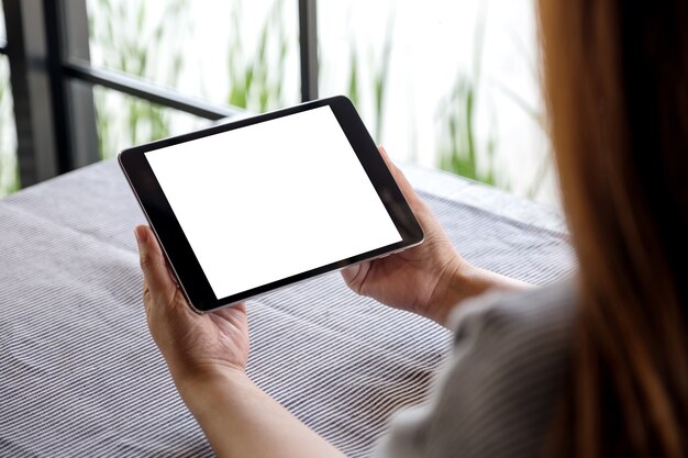 una mujer que sostiene la PC de la tableta negro con pantalla de escritorio en blanco en la mesa de café