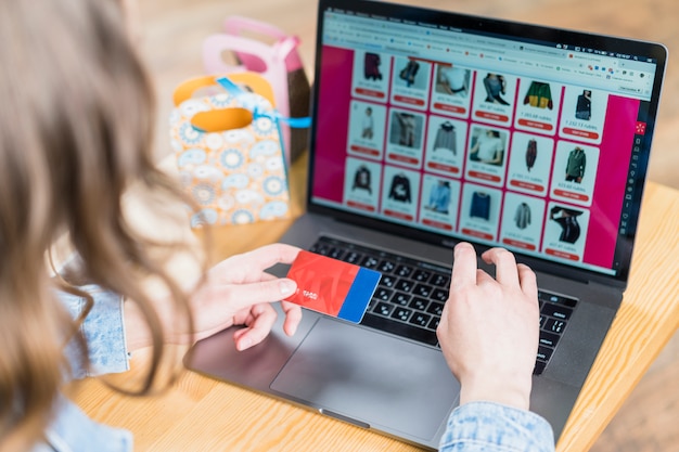 Foto mujer que sostiene la tarjeta de crédito frente a la computadora portátil con el sitio web de compras