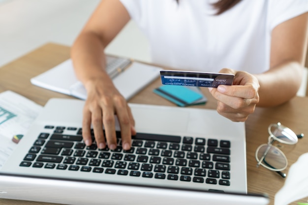 Mujer que sostiene la tarjeta de crédito y que usa el ordenador portátil del ordenador, la cuenta y el concepto de ahorro.