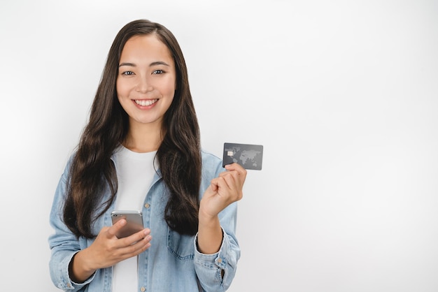 Mujer que sostiene la tarjeta de crédito y el teléfono móvil mientras mira la cámara aislada sobre el fondo blanco
