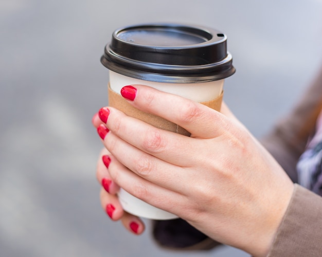 Mujer que sostiene la taza de café en la calle borrosa