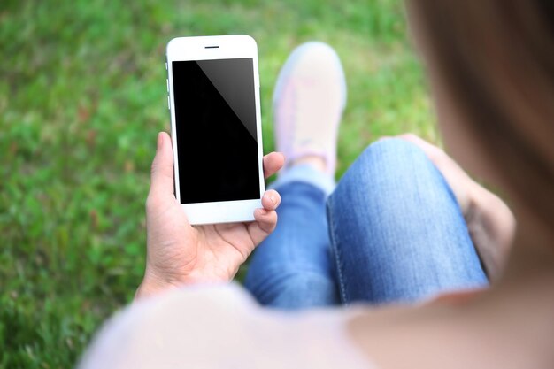 Mujer que sostiene el teléfono inteligente en el fondo de hierba borrosa