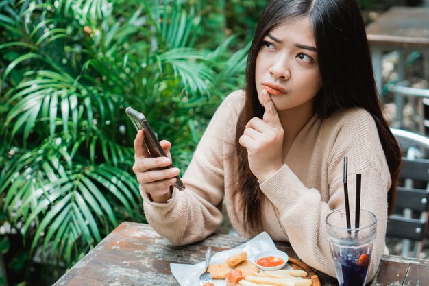 Mujer que sostiene el teléfono inteligente mientras piensa