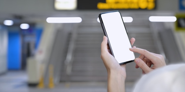 Mujer que sostiene el teléfono inteligente de pantalla en blanco en la estación de tren