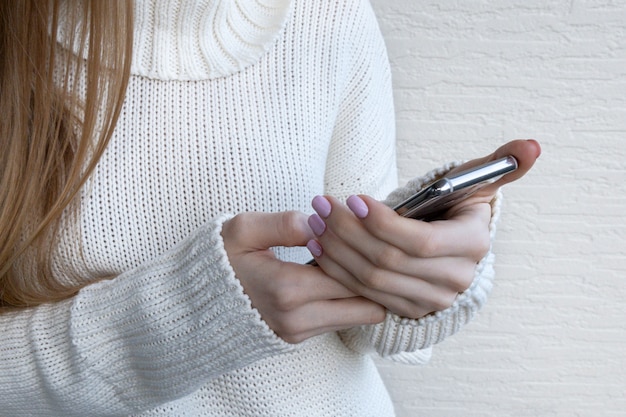 Mujer que sostiene el teléfono móvil moderno en fondo claro.