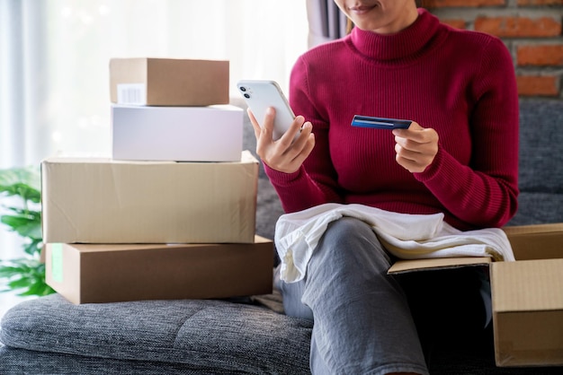 Una mujer que sostiene el teléfono y utiliza una tarjeta de crédito para realizar un pedido de compras en línea