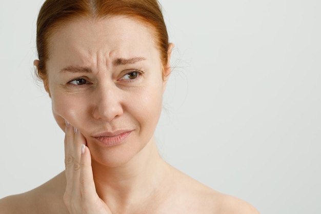 Una mujer que sufre de dolor de dientes fuertes tocando la mejilla con el concepto de odontología de la mano