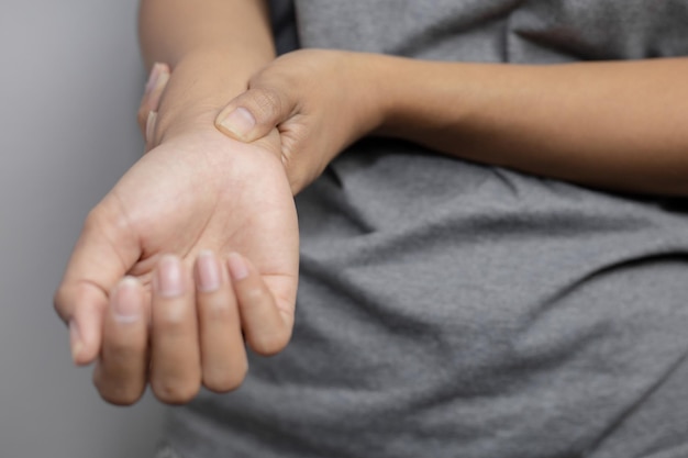 Mujer que sufre de dolor en la muñeca. Dolor en la muñeca de una mujer. Mujer joven sosteniendo su muñeca dolorosa sobre fondo de pared.