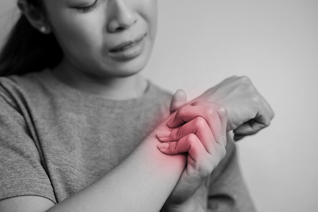 Mujer que sufre de dolor en la muñeca. Dolor en la muñeca de una mujer. Mujer joven sosteniendo su muñeca dolorosa sobre fondo de pared.