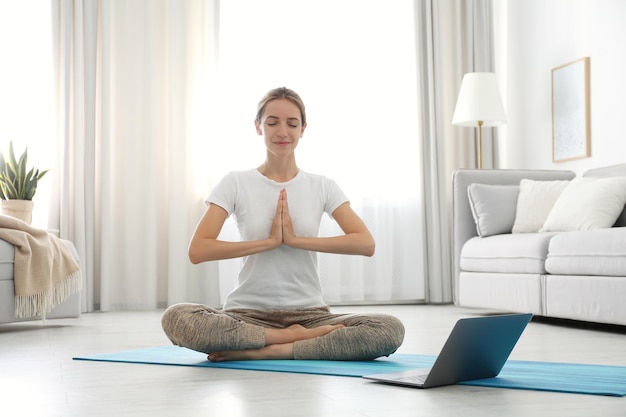 Mujer que tiene una clase de video en línea a través de una computadora portátil en casa Curso de yoga a distancia durante la pandemia de coronavirus