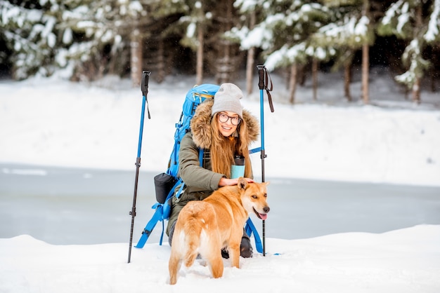 Mujer que tiene un descanso durante el invierno senderismo acariciando a su perro en las montañas nevadas cerca del lago y el bosque