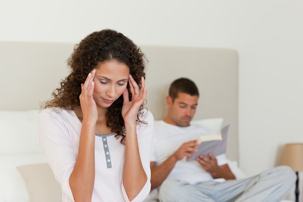 Foto mujer que tiene un dolor de cabeza mientras su marido está leyendo